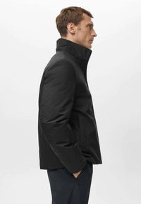 Giacca nera imbottita con colletto alto, texture liscia e cerniera frontale. Presenta tasche laterali e una silhouette aderente.