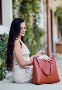 Braune Lederhandtasche mit geschwungenem Design, verstellbarem Schulterriemen und glatter Textur. Hervorzuheben ist der minimalistische Stil und das dezente Logo.