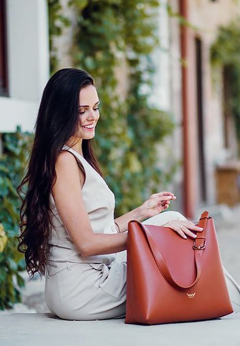 Braune Lederhandtasche mit geschwungenem Design, verstellbarem Schulterriemen und glatter Textur. Hervorzuheben ist der minimalistische Stil und das dezente Logo.
