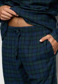 Pajama set w kratkę w ciemnym niebieskim i zielonym kolorze, z elastycznym pasem, sznurkiem i kieszeniami. Miękka tekstura i luźny krój.