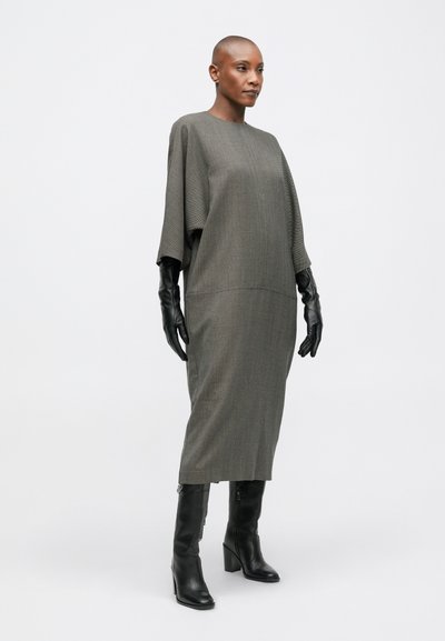 Hosszú, szürke, kötött ruha magas nyakkivágással és denevérujjakkal. Fekete, testhez simuló bőrkesztyűkkel és térdig érő fekete magassarkú csizmával párosítva.