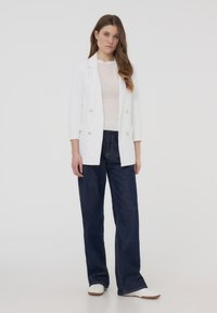 Biała podwójnie zapięta marynarka na lekki sweter, w połączeniu z ciemnoniebieskimi szerokimi spodniami dżinsowymi i białymi trampkami. Gładki materiał, strukturalny design.