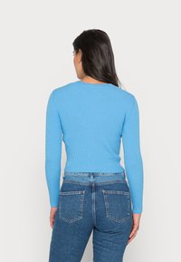 Ribbet genser med lange ermer i ensfarget lyseblå, tettsittende design, med rund hals og kombinert med høyt liv blå jeans.