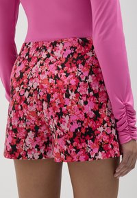 Shorts floreali con sfondo nero caratterizzati da fiori rosa e rossi. Design a vita alta con una consistenza liscia e una vestibilità aderente.