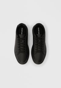 Ζευγάρι μαύρα αθλητικά παπούτσια με κορδόνια και απλό σχεδιασμό, σε λευκό φόντο, απεικονιζόμενα από επάνω.