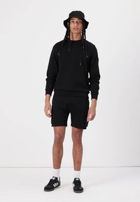 Sort sweatshirt og shorts sæt med afslappet pasform, ribbede manchetter og en bucket hat. Sorte sneakers med hvide detaljer fuldender looket.