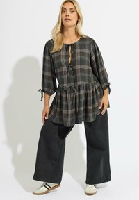 Blusa de cuadros oscuros con un corte holgado, cintura fruncida y escote atado. Combinada con jeans negros de pierna ancha y zapatillas blancas.