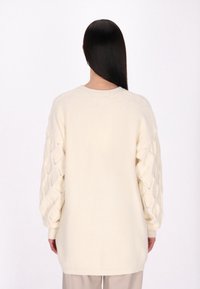Langärmliger cremefarbener Pullover mit strukturiertem Zopfmuster an den Ärmeln, mit lässiger Passform und rundem Halsausschnitt. Weiches, gemütliches Strickmaterial.