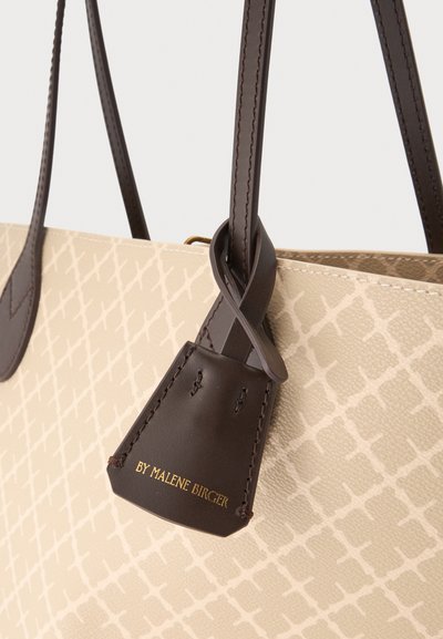 Sac à main beige à motif avec anses en cuir brun foncé et étiquette embossée "BY MALENE BIRGER" en lettres dorées.