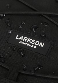 Fekete szövet táska vízcseppekkel, egy téglalap alakú fekete címkével, fehér felirattal: "LARKSON HAMBURG." Texturált anyag, varrási részletekkel.