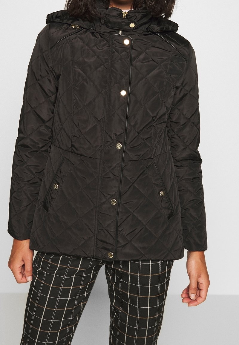 Svart vadderad jacka med huva, utrustad med guldfärgad maskinvara, tryckknappar och två framfickor. Strukturerat tyg med diamantmönster.