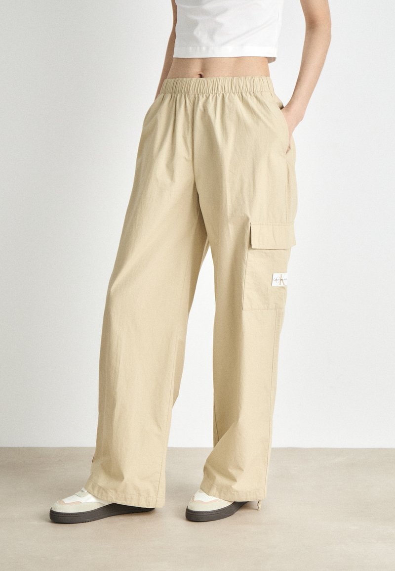Beige cargobroek met een elastische tailleband, zijzakken en een opgestikte zak op de dij. Gemaakt van lichtgewicht stof met een relaxte pasvorm.