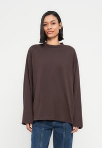 Καφέ μακρυμάνικο τοπ, κατασκευασμένο από μαλακό υλικό, με στρογγυλή λαιμόκοψη και άνετη εφαρμογή. Συνδυάζεται με μπλε τζιν. Απλός σχεδιασμός, χωρίς σχέδια.