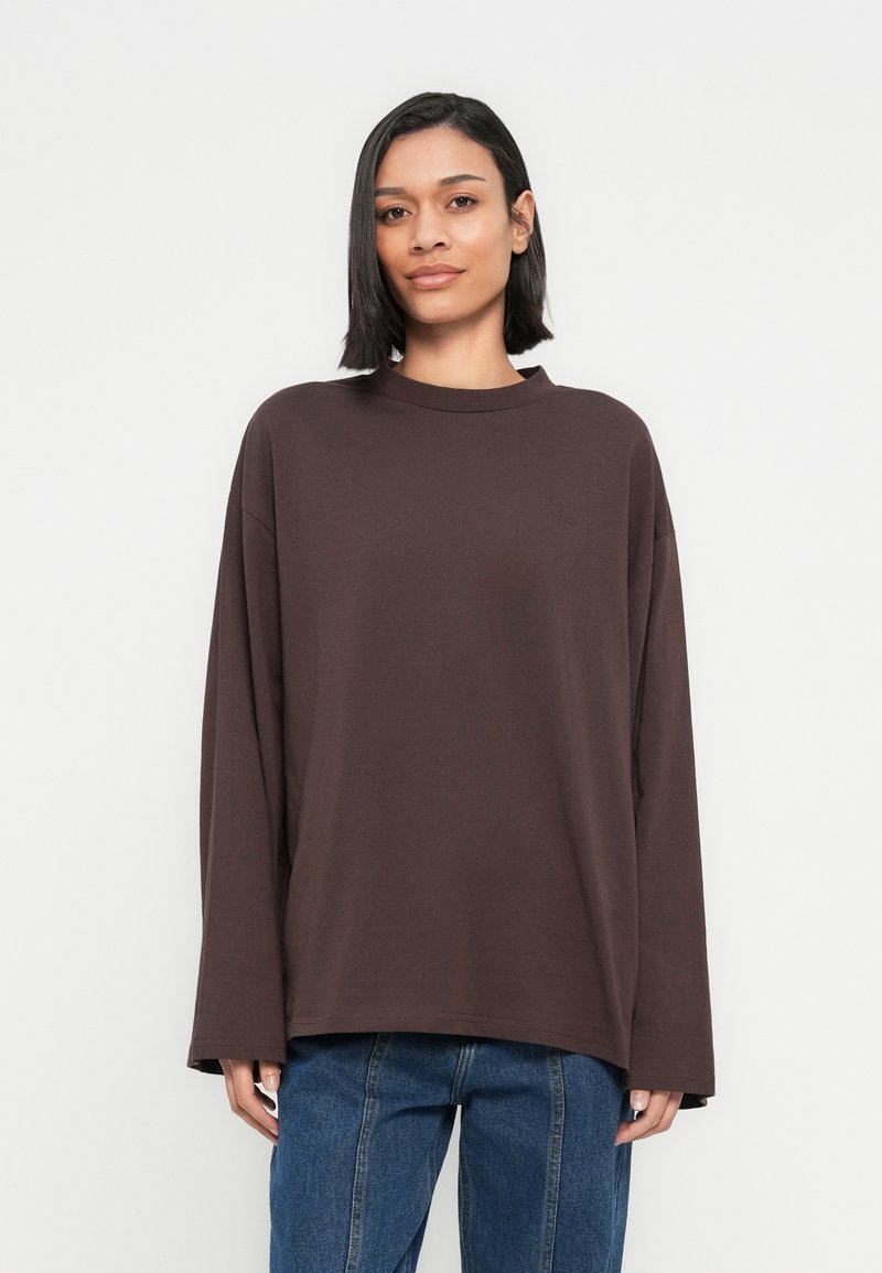 Καφέ μακρυμάνικο τοπ, κατασκευασμένο από μαλακό υλικό, με στρογγυλή λαιμόκοψη και άνετη εφαρμογή. Συνδυάζεται με μπλε τζιν. Απλός σχεδιασμός, χωρίς σχέδια.