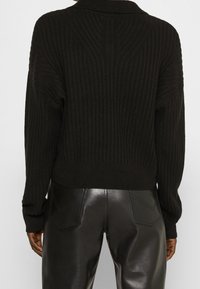 Suéter de punto negro acanalado con un cuello alto, que presenta mangas largas y una silueta ajustada, combinado con pantalones de cuero negro de tiro alto.