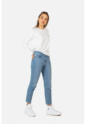 Lightweight white long-sleeve shirt with a small logo, paired with light blue denim jeans and white high-top sneakers.