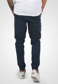 Navyblå joggerbyxor med elastiska mudd, gjorda av mjukt material; bärs med vita sneakers, minimalistisk design, inga synliga mönster.