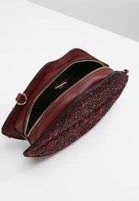 Bordowa skórzana torba na ramię z błyszczącym czarnym dnem, zamykana na zamek błyskawiczny, z złotymi akcentami. Wnętrze wyścielone czarną podszewką.