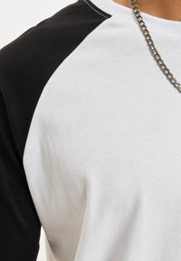 Kortärmad raglan t-shirt med vit kropp och svarta ärmar, tillverkad av bomull med en slät textur och rund halslinning.