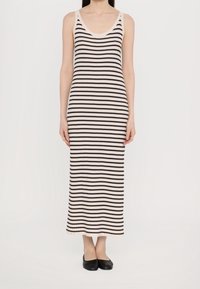 Robe maxi en tricot à rayures crème et noir, avec un décolleté rond et une texture côtelée. Longueur au sol, sans manches, portée avec des ballerines noires.