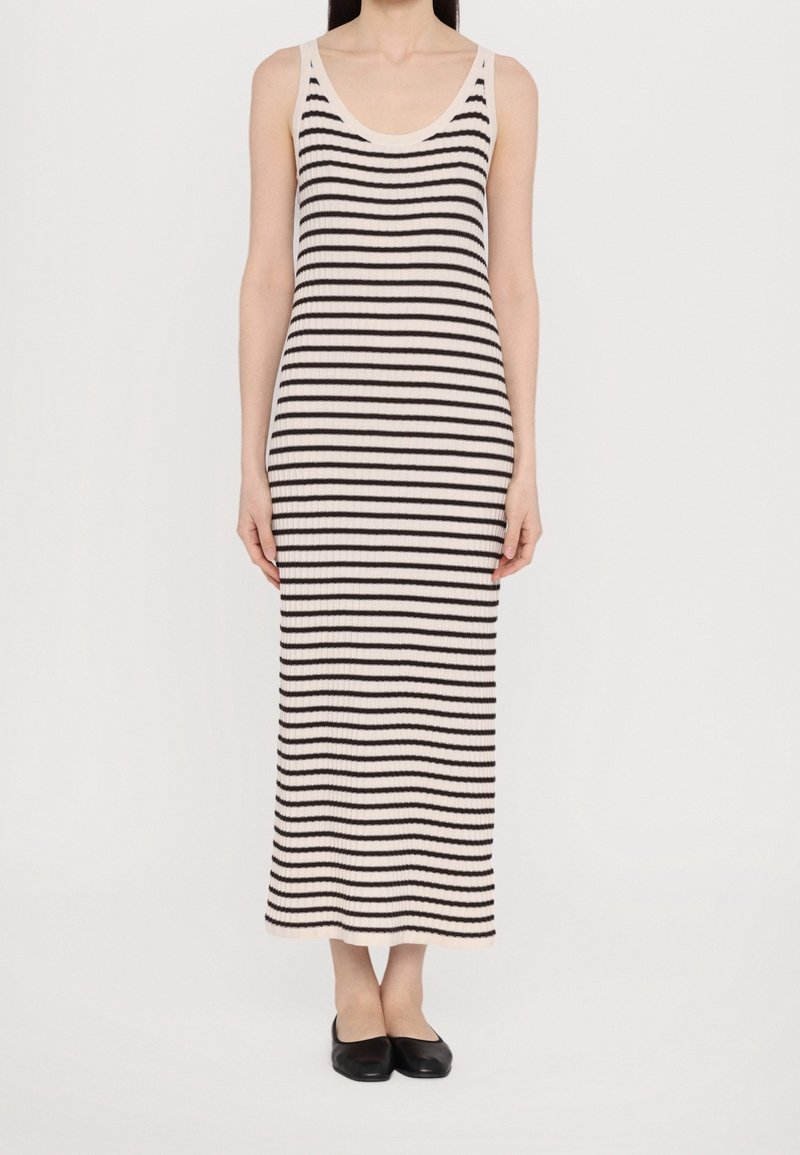 Robe maxi en tricot à rayures crème et noir, avec un décolleté rond et une texture côtelée. Longueur au sol, sans manches, portée avec des ballerines noires.
