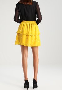 Gonna gialla a strati con una vita smock, caratterizzata da un sottile motivo a pois. Indossata con un top nero a maniche lunghe e tacchi neri.