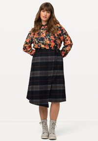 Dunkelblauses, langärmliges Hemd mit orangefarbenen Blumen, kombiniert mit einem karierter, knielanger Rock in Schwarz und Grau mit roten Akzenten. Graue Schnürboots.