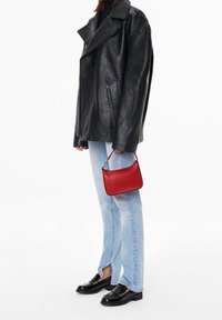 Veste en cuir noire avec grand col, jeans bleu clair, et un petit sac à main en cuir rouge avec une anse chaîne. Des mocassins noirs complètent le look.