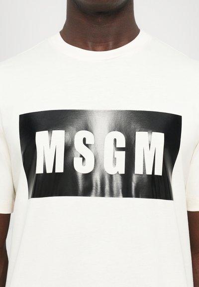 Balta medvilnės marškinėliai su ryškiu juodu stačiakampiu grafiku, kuriame baltais raidėmis užrašyta "MSGM". Lygus paviršius, trumpomis rankovėmis.