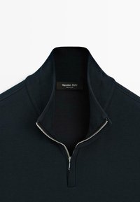 Zwarte ritspull met hoge kraag en zilveren rits. Gladde stoftextuur; voorzien van een label met "Massimo Dutti" aan de binnenkant van de hals.