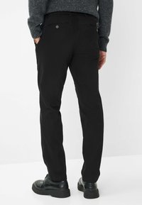 Pantaloni in cotone neri con vestibilità dritta, dotati di tasche posteriori, dettagli di cucitura discreti e indossati con scarpe nere su uno sfondo bianco.