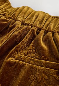 Tela de terciopelo marrón con una textura rica, que presenta un patrón floral y detalles fruncidos. Un brillo sutil realza su atractivo visual.