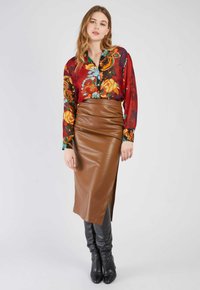  rote Bluse mit floralen Mustern und langen Ärmeln, kombiniert mit einem braunen Leder-Midirock mit einem seitlichen Schlitz und kniehohen schwarzen Lederstiefeln.