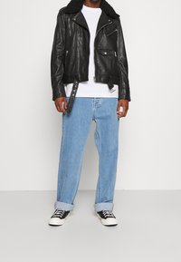 Sort læder bikerjakke med pelskrave, parret med lys blå jeans og sorte sneakers. Jakken har flere lynlåse og lommer.