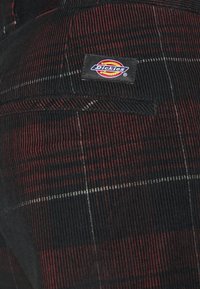 Tkanina w czarno-czerwone paski z dodatkową kieszonką i metką marki "Dickies", prezentująca teksturowany, żeberkowy wzór.