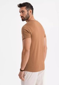 Krátký rukáv, přiléhavé tričko z jemné hnědé bavlny, s kulatým výstřihem, hladká textura, s hladkým zadním dílem a minimálními švy.