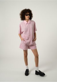 Kortermet rosa stripete skjorte og matchende shorts, laget av lett stoff. Kombinert med svarte platåskjønner og hvite sokker.