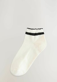 Witte katoenen enkelsok met een ribbelrand die twee horizontale zwarte strepen heeft. Soepele textuur, afgeronde teen en een nauwsluitend ontwerp.