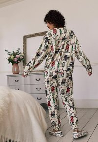 Conjunto de pijama crema con estampados de animales en negro, rojo y verde. Camiseta y pantalones de corte holgado, textura suave, pantuflas a juego, diseño cohesivo.