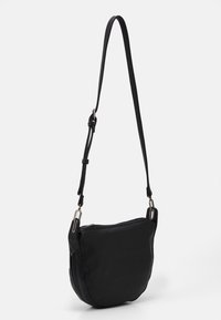 Černá crossbody taška vyrobená z jemného materiálu, se zaobleným tvarem, nastavitelným popruhem a kovovými akcenty. Hladký povrch.