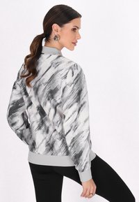 Jachetă bomber cu un model abstract în nuanțe de gri și alb, cu manșete și tiv elastic, având o croială lejeră și mâneci lungi.