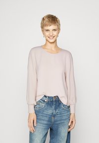 Light pink long-sleeve top with a round neckline and balloon sleeves, paired with high-waisted blue denim jeans. Smooth fabric texture.