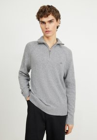 Sweatshirt gris zippé avec un tricot texturé, des poignets et un ourlet côtelés. Présente une fermeture éclair d'un quart de longueur et un petit logo sur la poitrine.