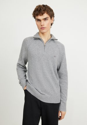 Sudadera gris con cremallera y un tejido texturizado, con puños y dobladillo de canalé. Presenta una cremallera de longitud cuartilla y un pequeño logo en el pecho.