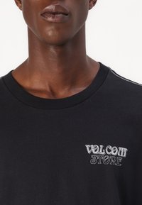 Black cotton t-shirt featuring a white embroidered "VOLCOM STORE" logo on the chest, rounded crew neckline, and short sleeves.
