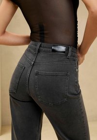 Haut en maille noire ajusté, rentré dans un jean noir délavé à taille haute, coupe droite, avec poches arrière et passants de ceinture.