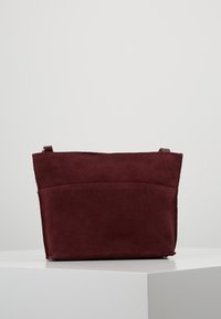 Burgundská semišová kabelka s obdélníkovým tvarem, jednoduchým designem a zadní kapsou. Obsahuje nenápadné horní zapínání.