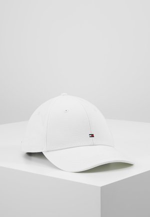Casquette de baseball blanche avec petit logo rectangulaire rouge, blanc et bleu à l'avant, posée sur une surface blanche en angle sur un fond gris.