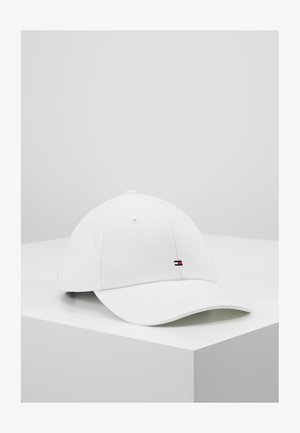 Weiße Baseballkappe mit kleinem rechteckigem roten, weißen und blauen Logo vorne, auf einer weißen Eckeoberfläche vor grauem Hintergrund platziert.