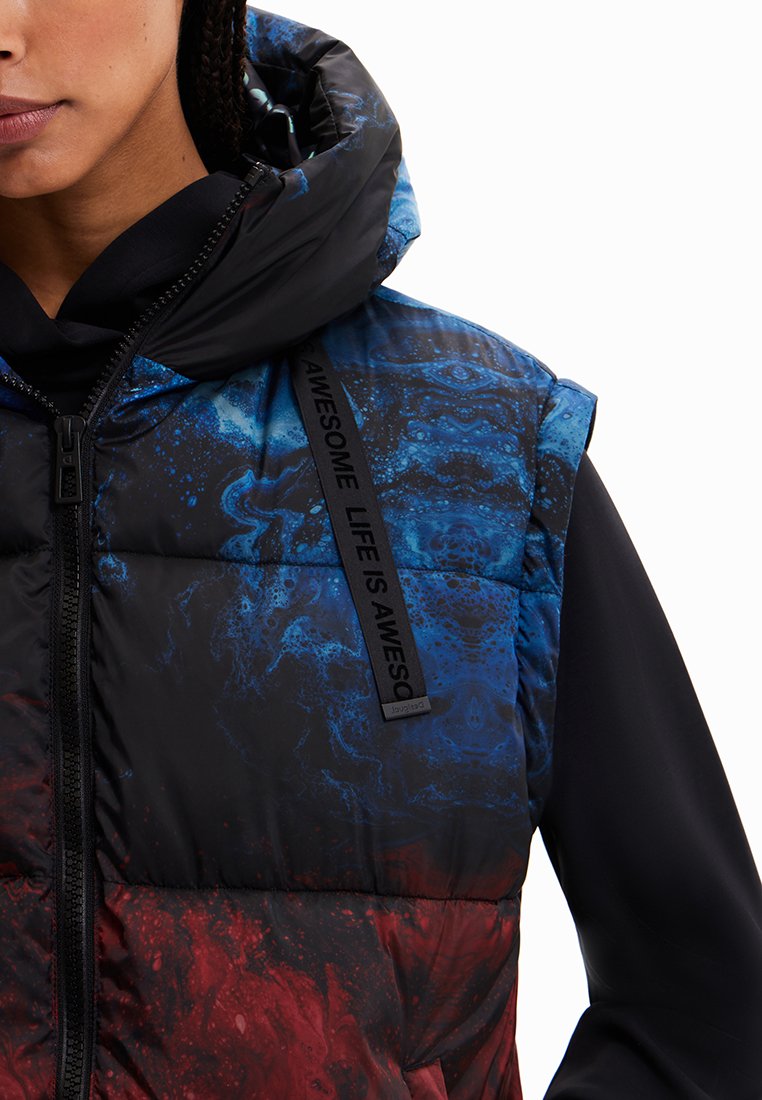 Gevoerde vest met een blauw en rood abstract patroon, zwarte kraag en opvallende rits. Bevat een zwarte stoffen band met tekst.